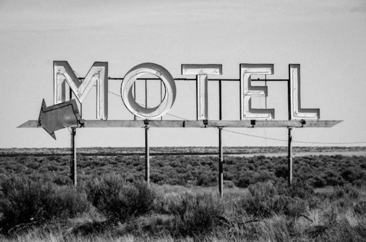 An old, weathered motel sign stands stark against a clear sky, indicative of the classic motels near major U.S. museums, offering a nostalgic slice of Americana.